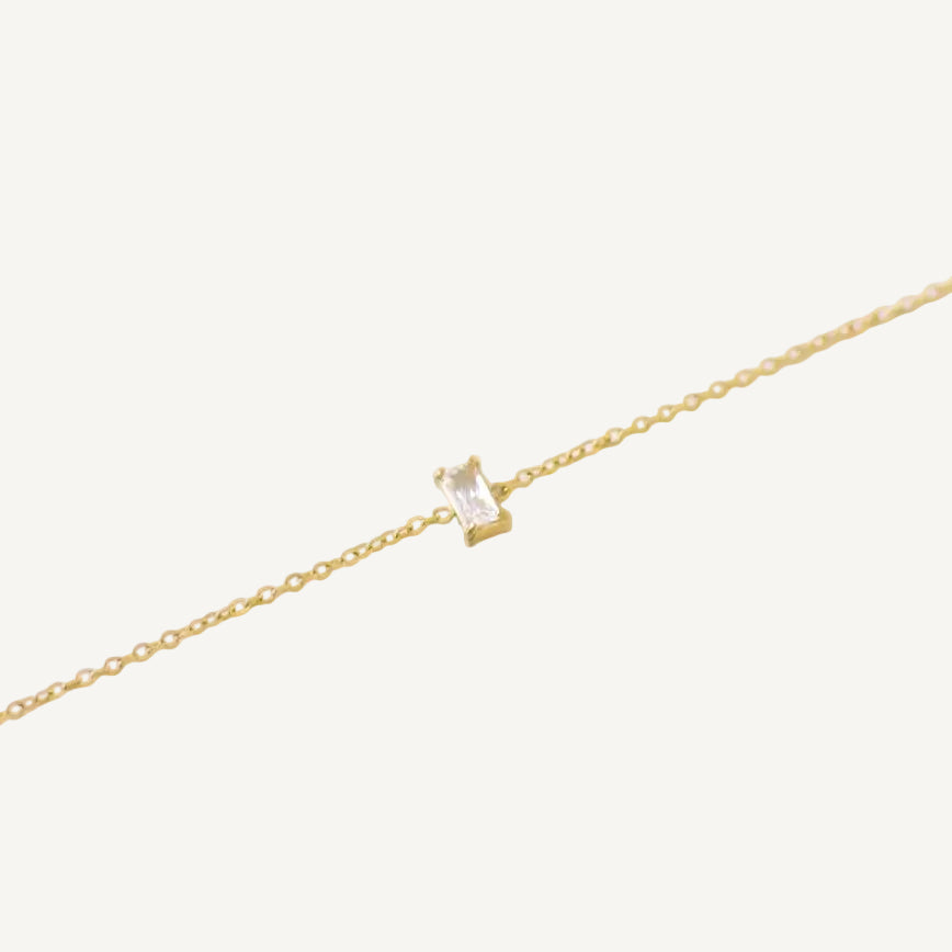 A gold-filled bracelet with a solid pattern and a small square-shaped charm in the center, on a white background.